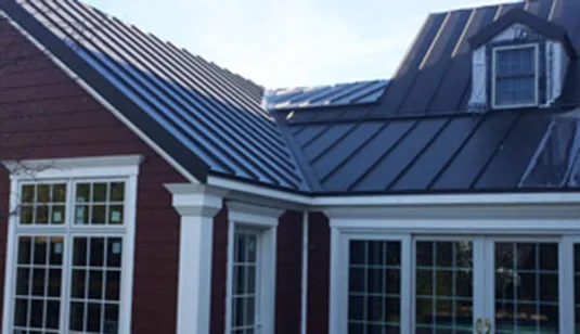 Gray standing seam roof and flashing where the roof meets the wall of a red house
